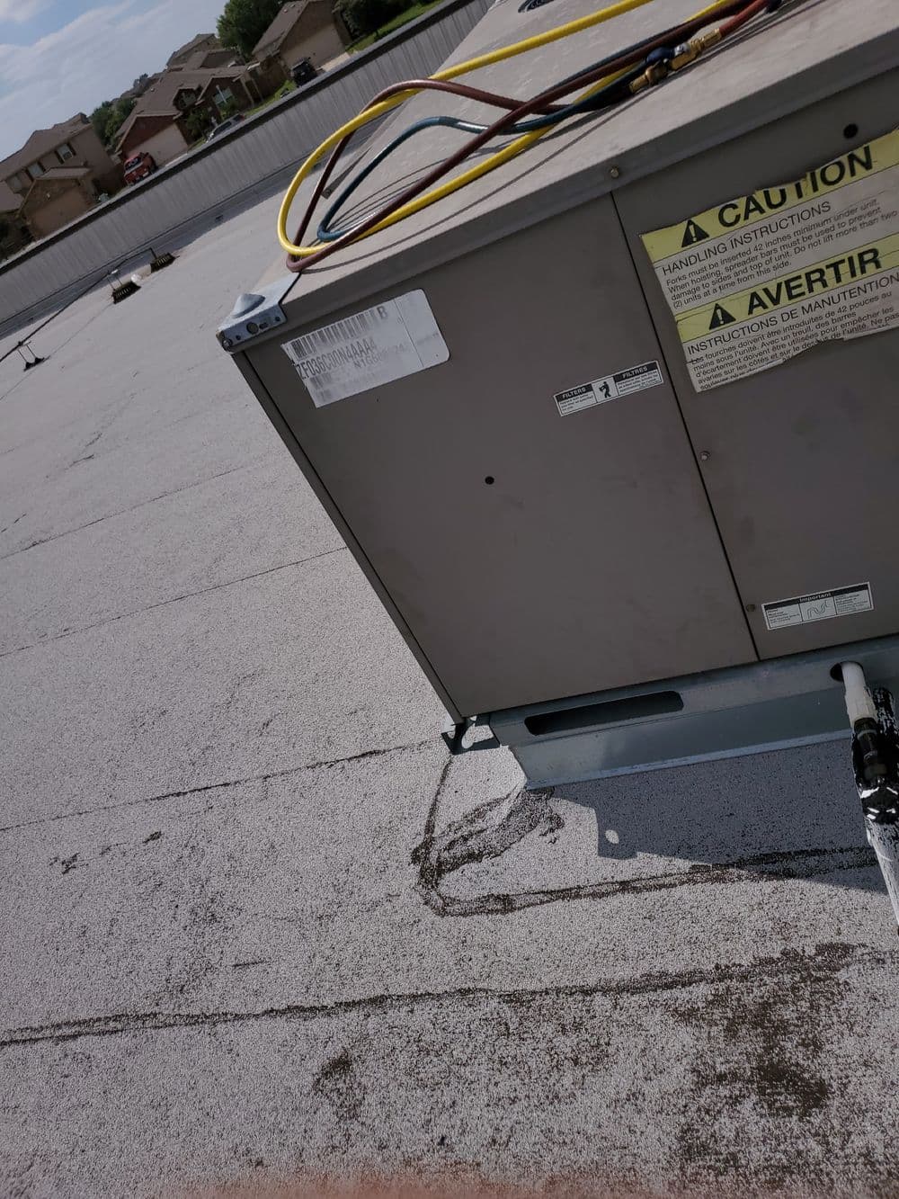 Commercial rooftop HVAC unit with caution signage on a flat roof.