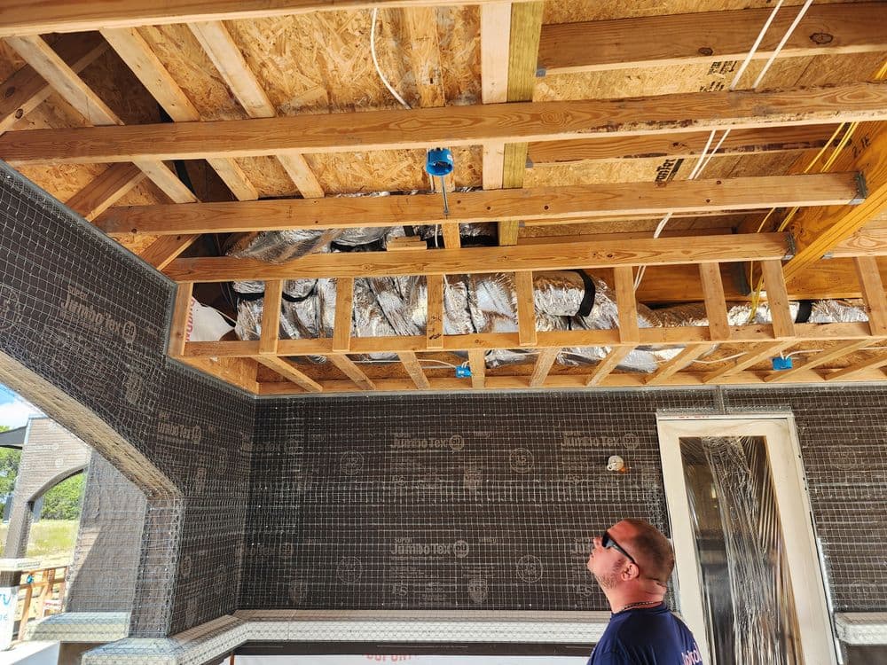 Home construction interior with exposed wooden beams and insulation, worker observing the ceiling.